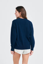 Brown haired female model wearing Jumper1234 Oversize cashmere vee neck cardigan in navy facing away from the camera