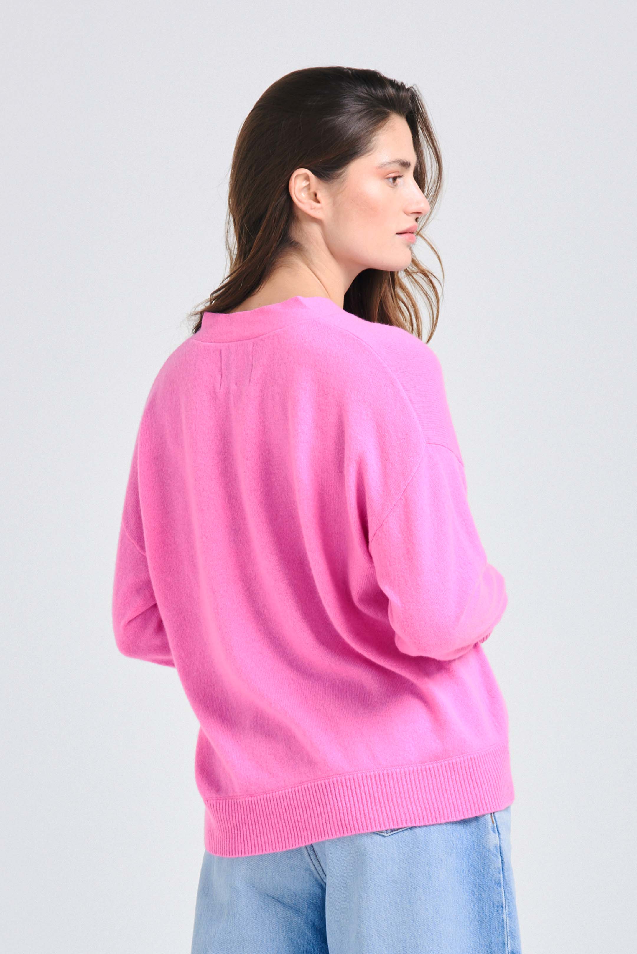 Brown haired female model wearing Jumper1234 Oversize cashmere vee neck cardigan in peony facing away from the camera
