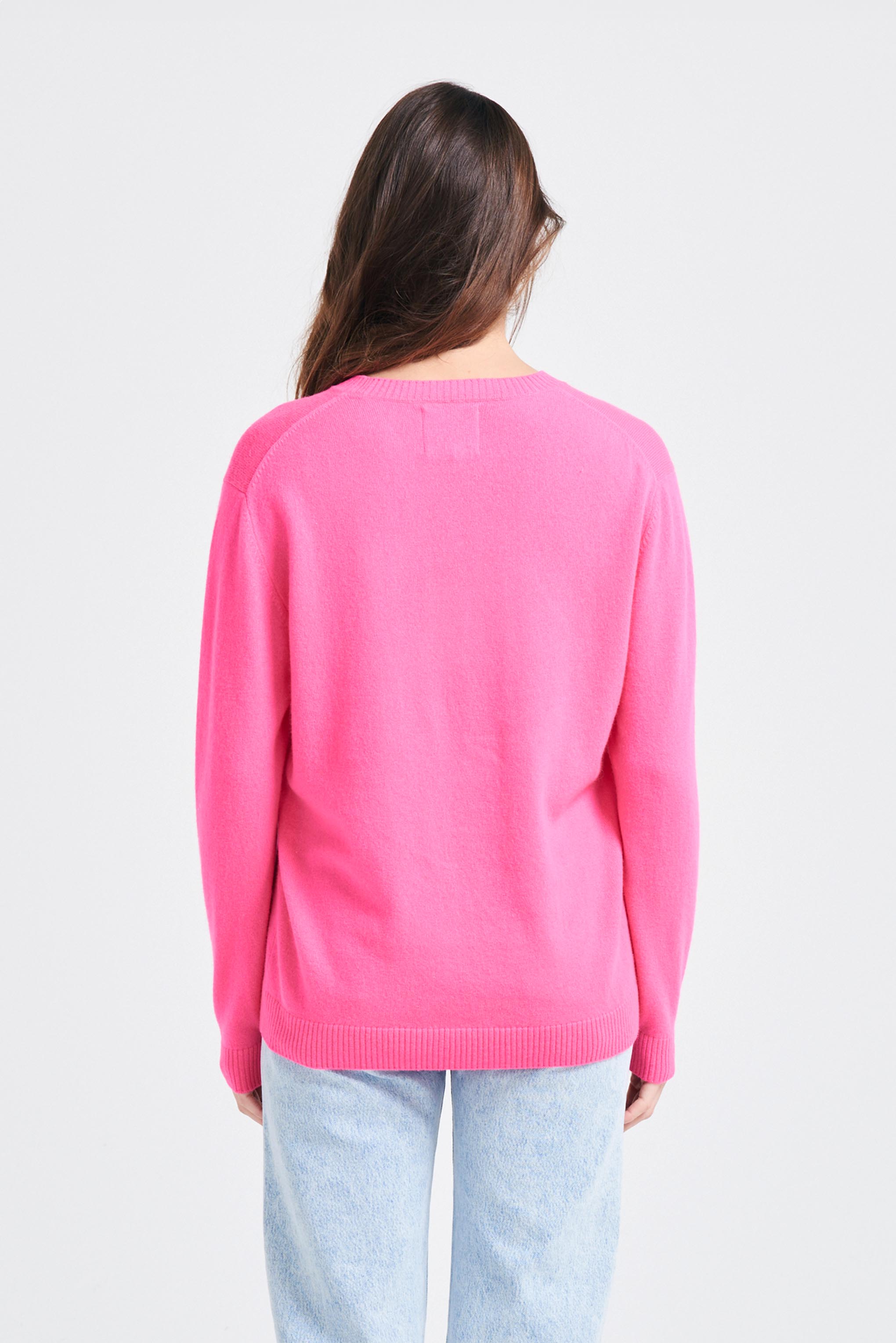 Brown haired female model wearing Jumper1234 Boyfriend fit cashmere crew neck jumper in neon pink facing away from the camera