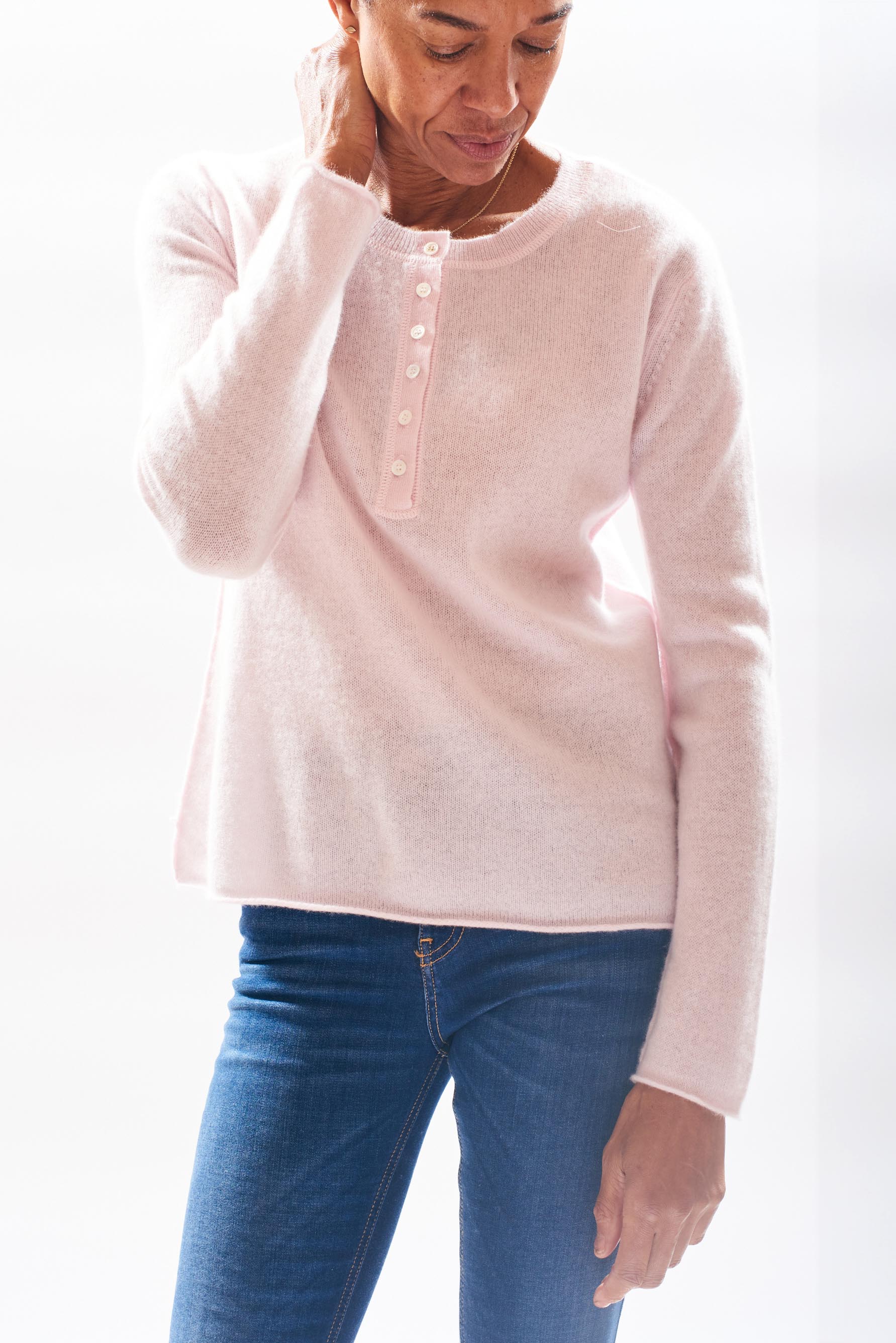 Model wearing Jumper 1234 cashmere henley in pale pink with a contrast gold stitching on the top button