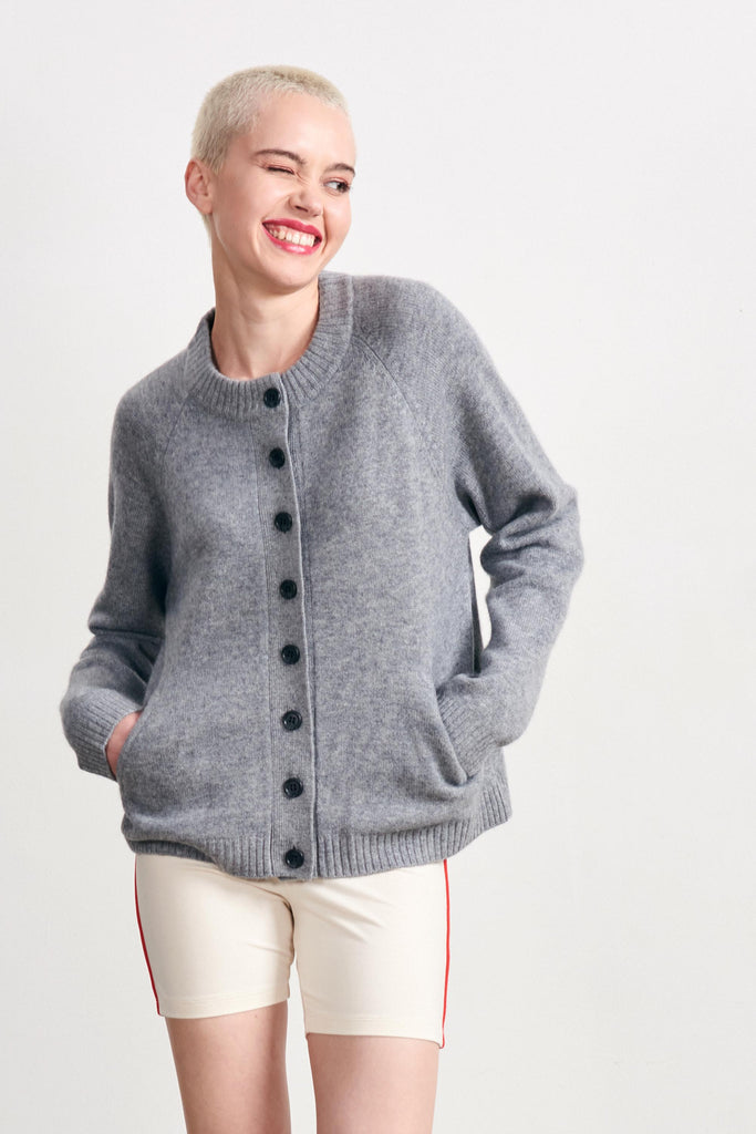 Blonde female model wearing Jumper 1234 mid grey heavier weight round neck cardigan in our cashmere and wool blend with stop and go intarsias on the elbows