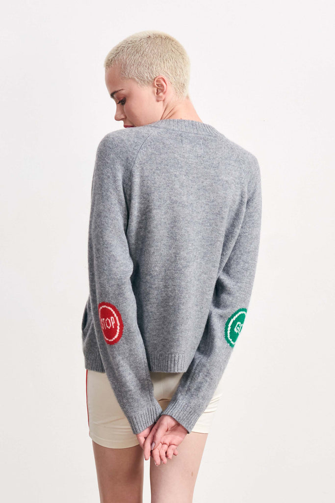Blonde female model wearing Jumper 1234 mid grey heavier weight round neck cardigan in our cashmere and wool blend with stop and go intarsias on the elbows facing away from the camera
