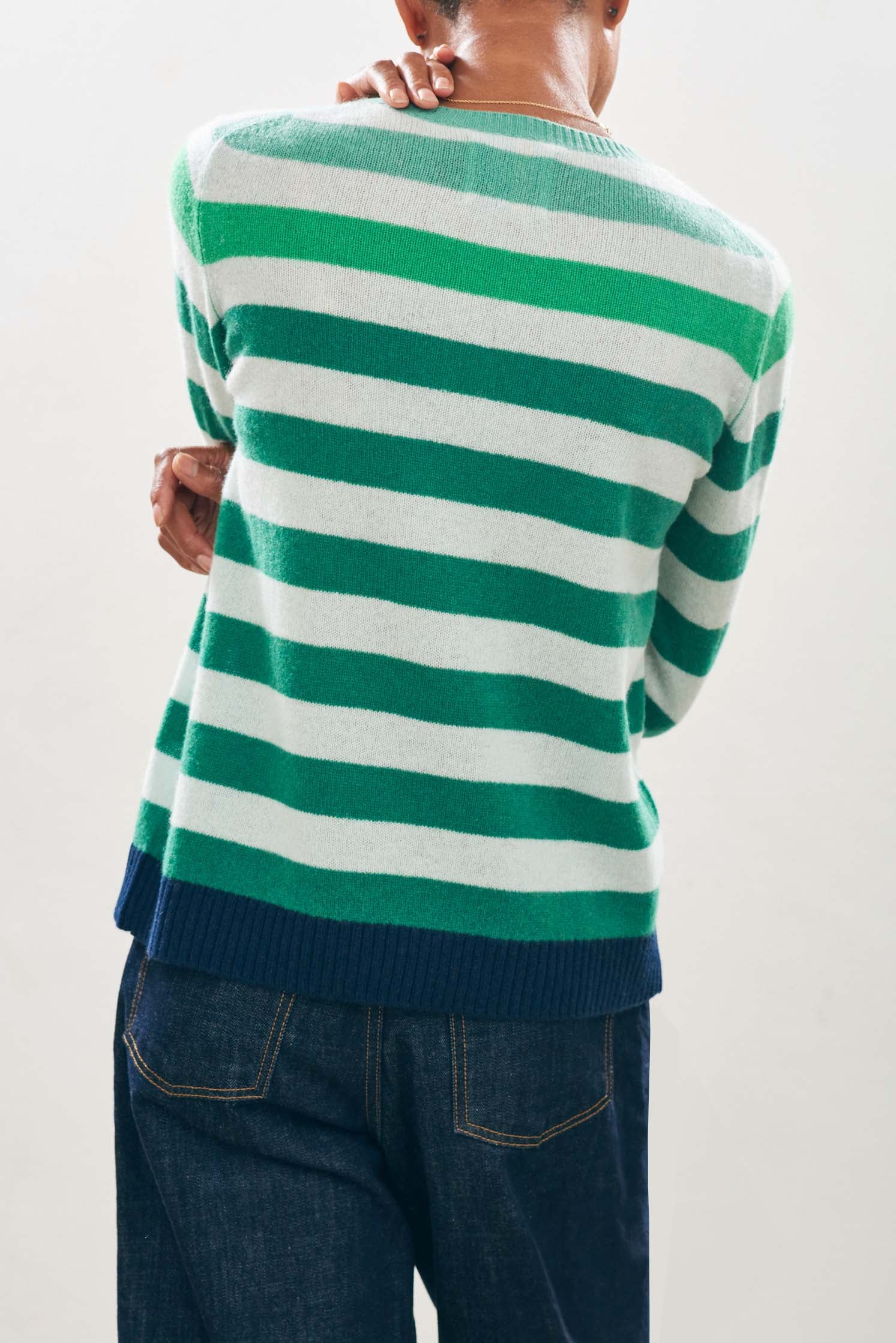 Female model wearing Jumper1234 Cashmere Gradient Stripe Crew in ombre shade of Green with navy ribs facing away from the camera