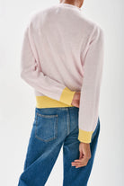 Model wearing Jumper 1234 cashmere pale pink vee neck cardigan with contrast lemon ribs facing away from the camera