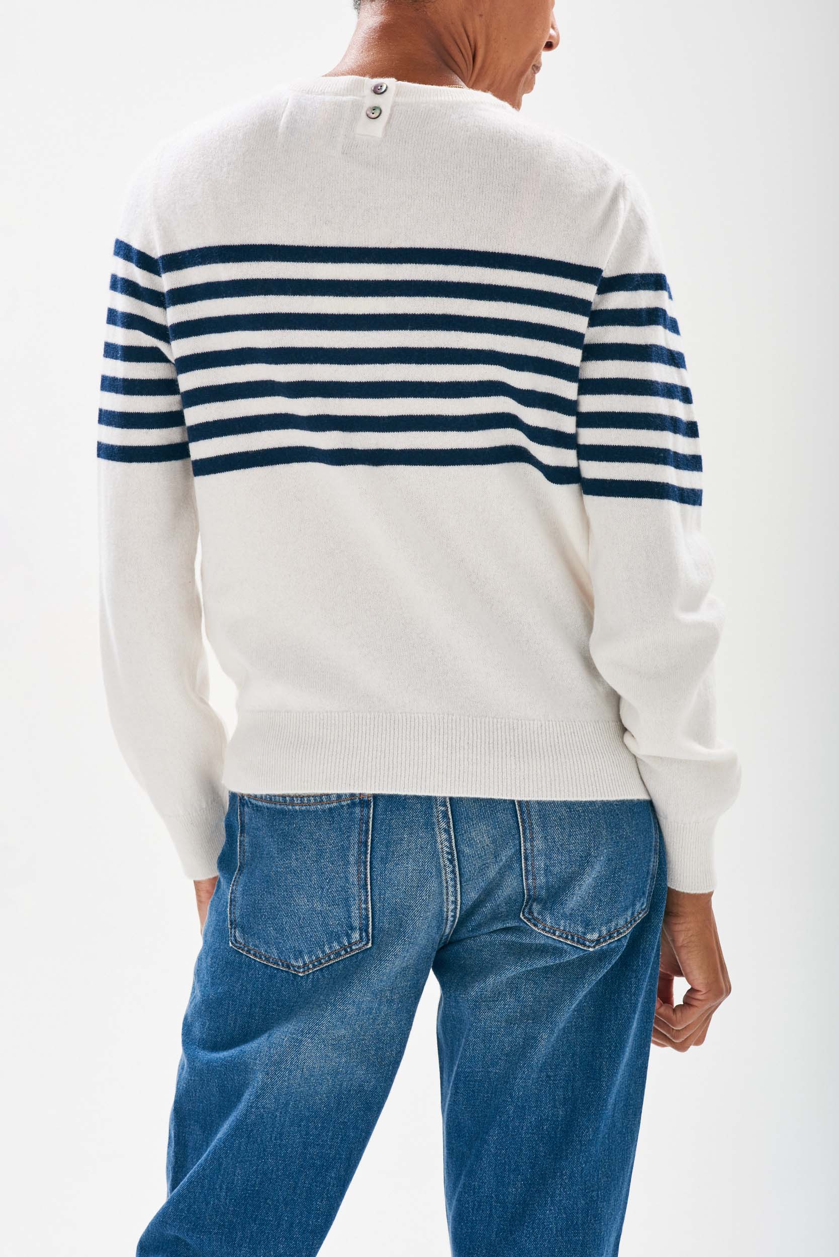 Model wearing Jumper1234 Cream cashmere crew neck jumper with navy stripe block running across the middle of the chest, with button detail at the back neck facing away from the camera