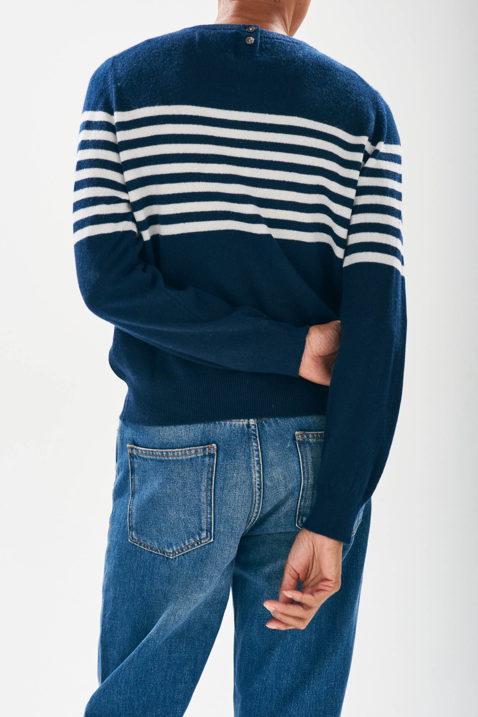 Model wearing Jumper1234 Navy cashmere crew neck jumper with cream stripe block running across the middle of the chest, with a button detail at the back neck facing away from the camera