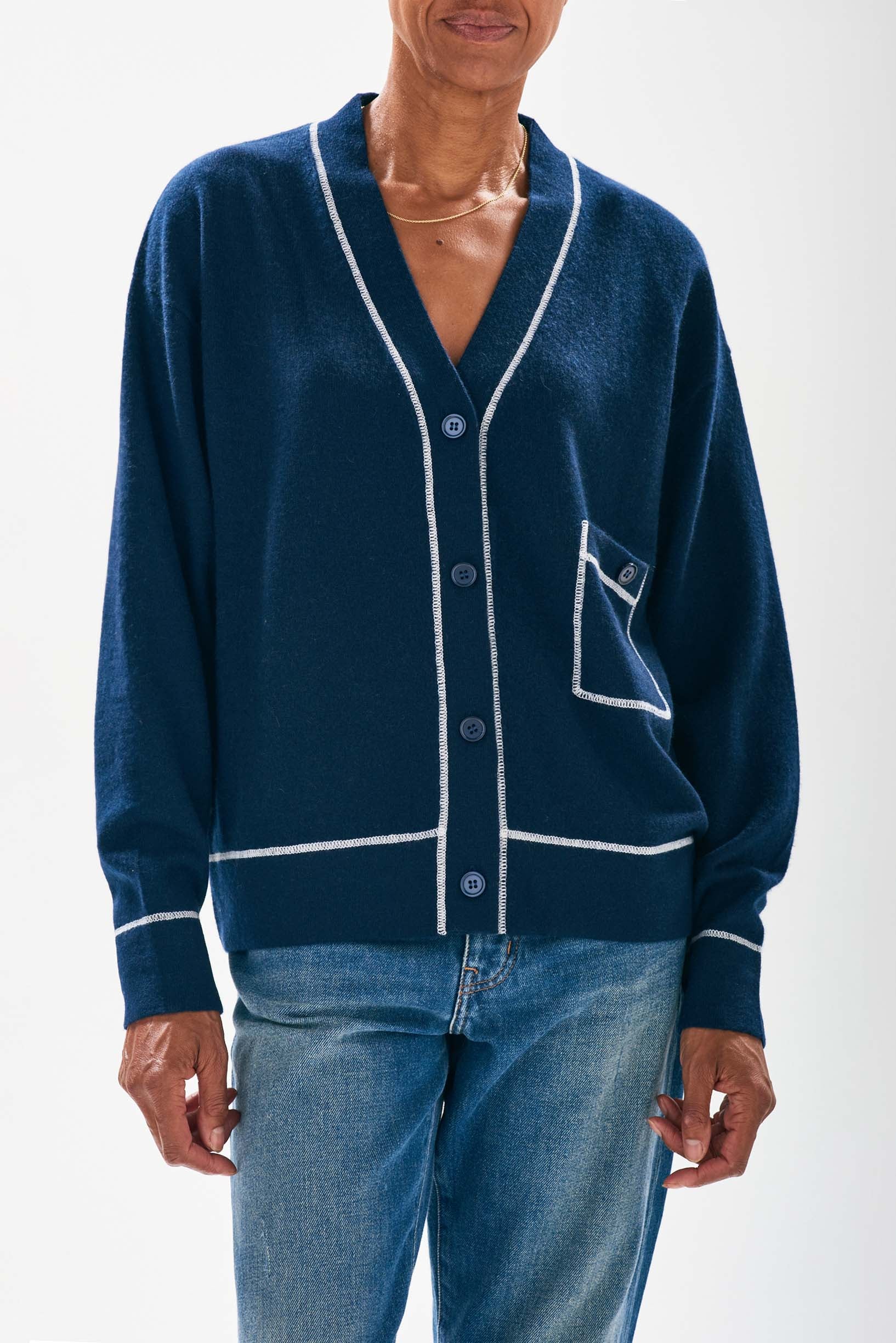 Model wearing Jumper1234 Navy boyfriend vee neck cashmere cardigan with cream top stitching detail and a pocket