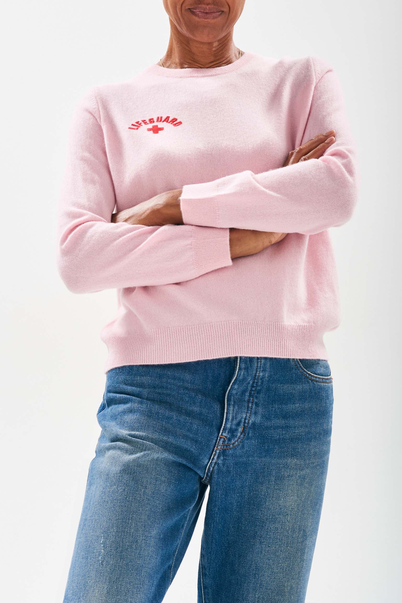 Model wearing Jumper1234 Pale pink cashmere crew neck jumper with red embroidered lifeguard detail