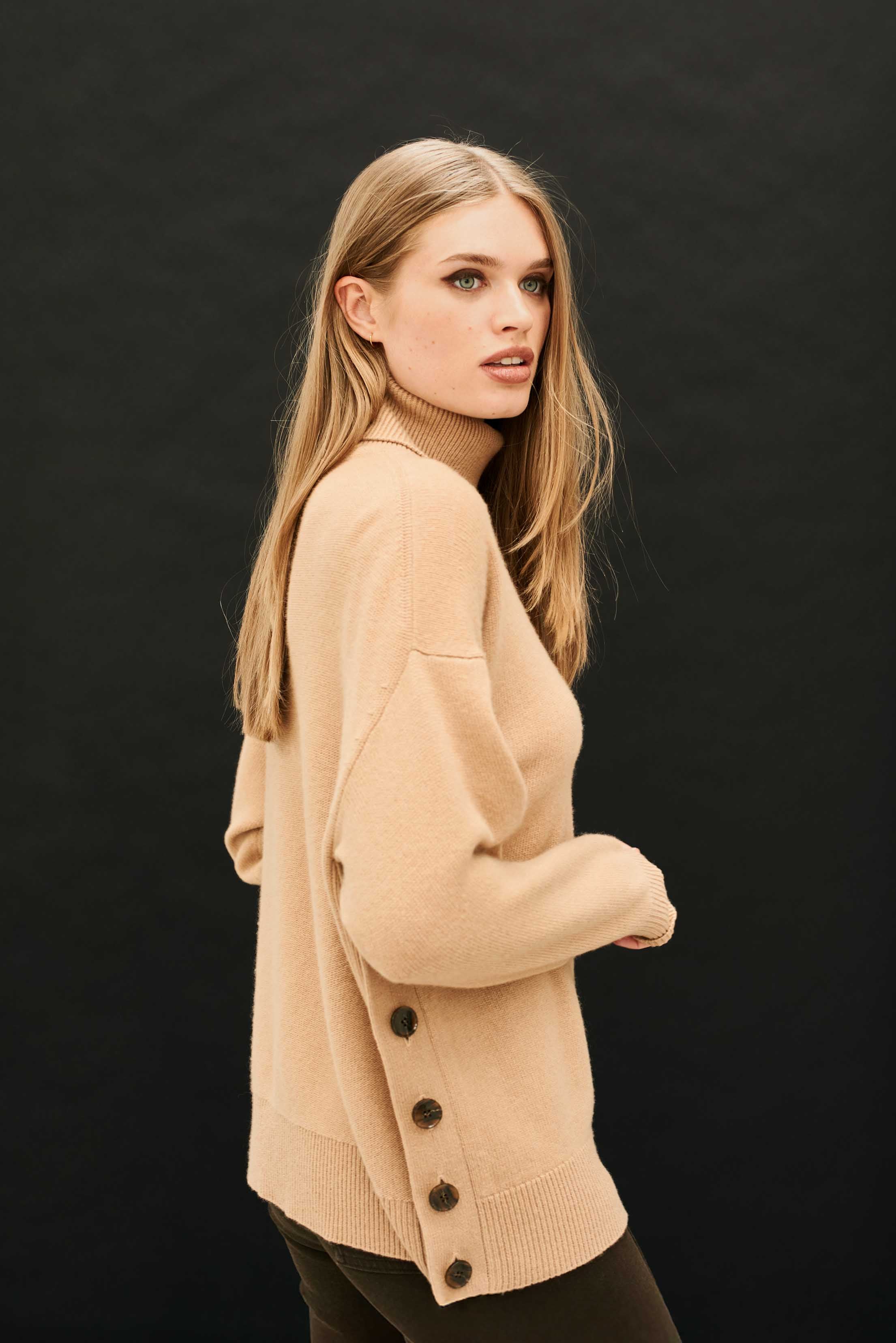 Female model wearing Jumper 1234 Oversize camel roll neck in our cashmere and wool blend, heavier weight with a great button detail on one side.