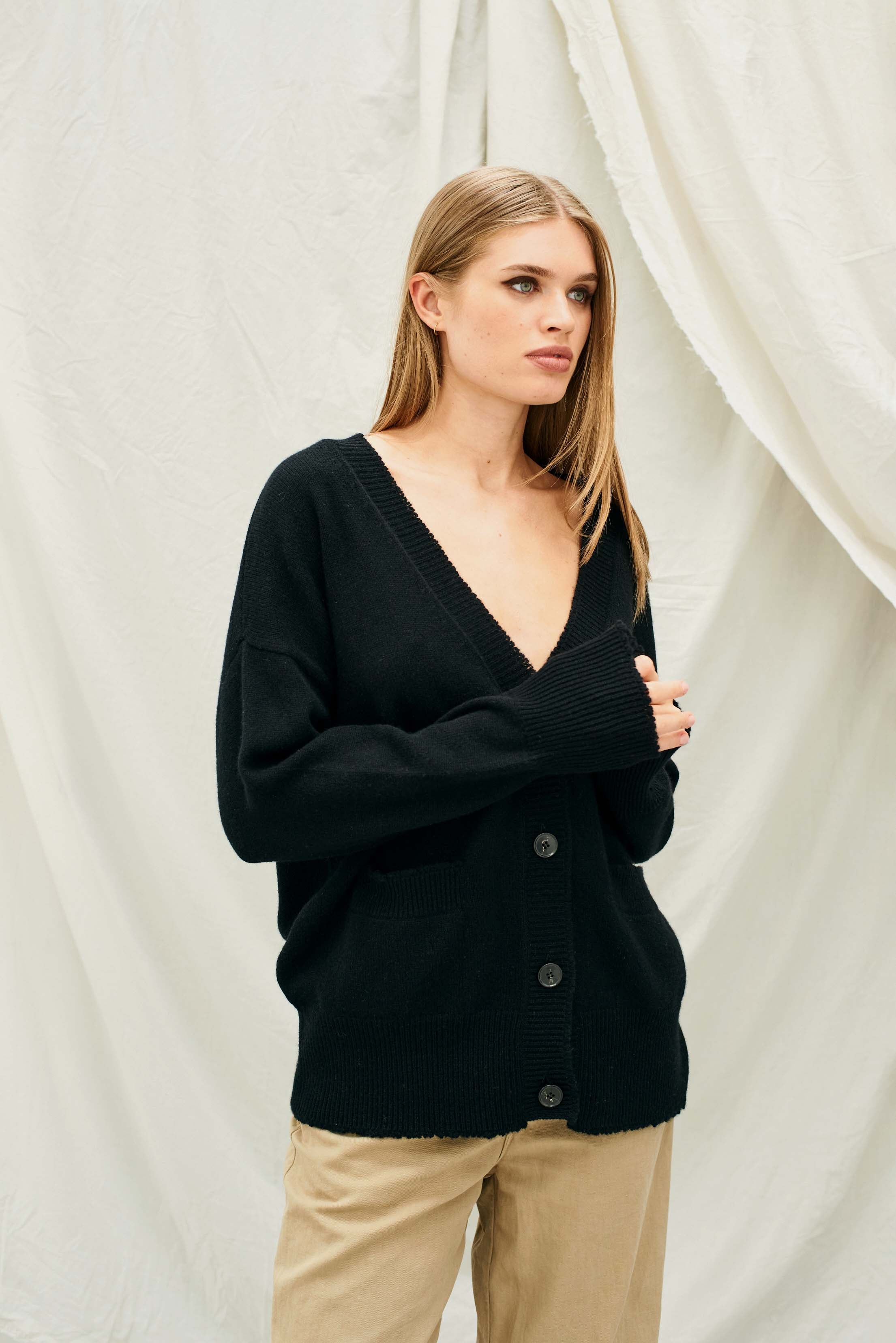 Female model wearing Jumper 1234 Heavier weight vee neck cardigan in black. Oversize fit with distressed ribs.
