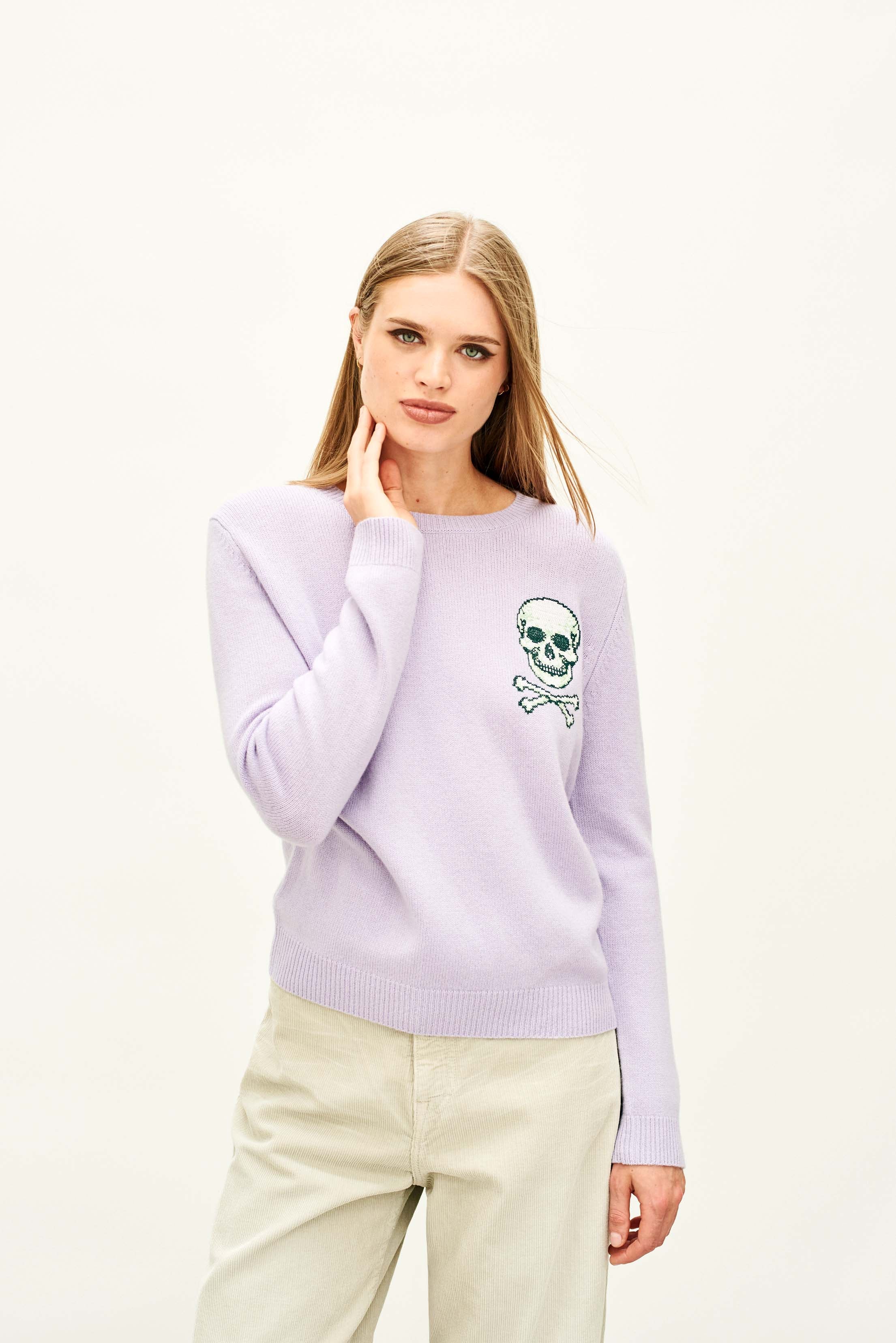 Female model wearing Jumper 1234 Lilac crew neck jumper in cashmere and wool, with an embroidered skull and crossbones on the chest.