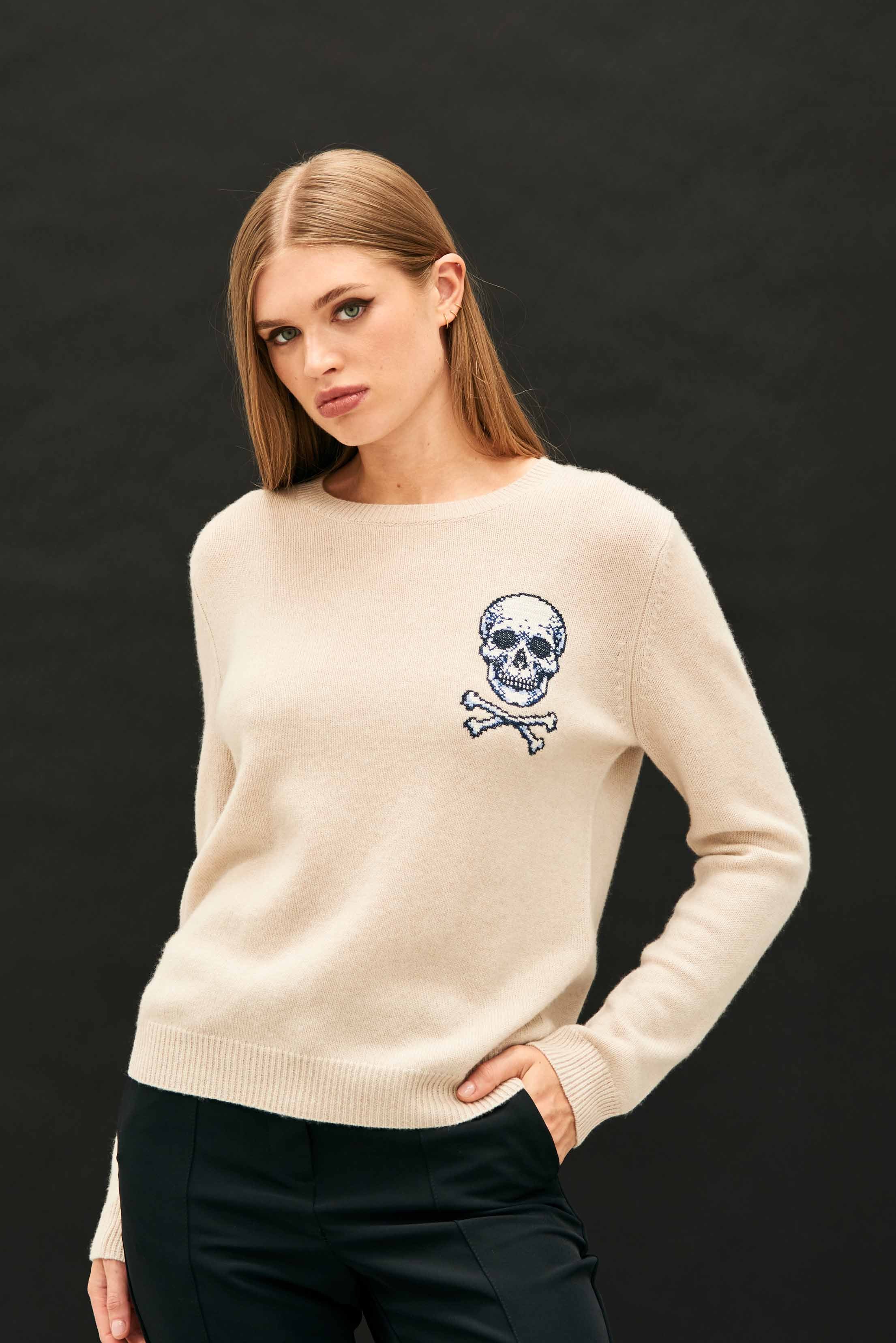 Female model wearing Jumper 1234 Stone crew neck jumper in cashmere and wool, with an embroidered skull and crossbones on the chest.