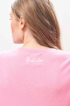 Female model wearing Jumper 1234 Candy cashmere crew neck jumper with cream 'naughty' chain stitch embroidery on the chest and 'but nice' on the back. Back shot