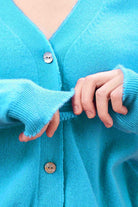 Blonde female model wearing Jumper 1234 Turquoise cashmere vee neck cardigan with 'distressed' ribs close up