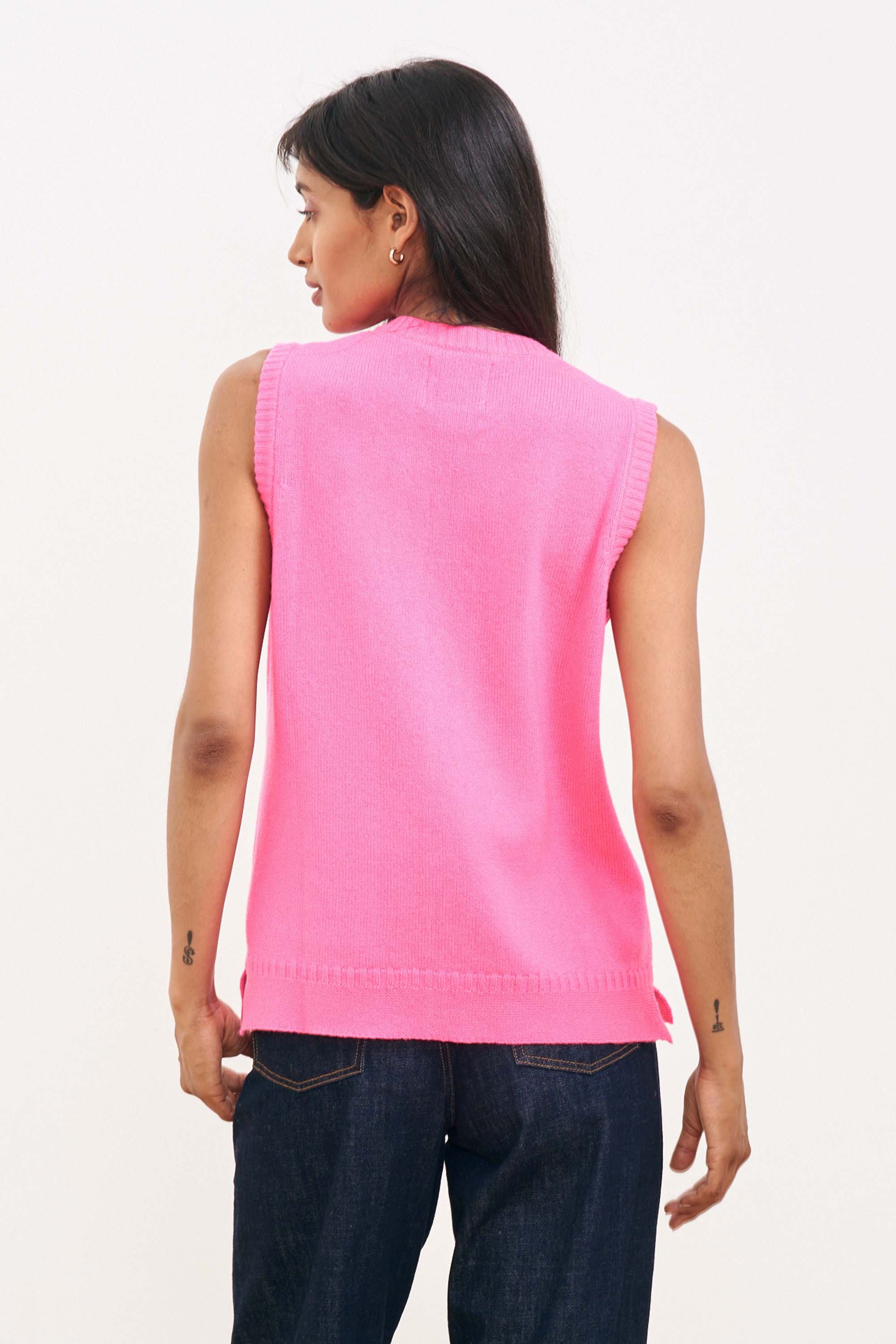 Brown haired female model wearing Jumper1234 neon pink cashmere sleeveless guernsey cardigan facing away from the camera
